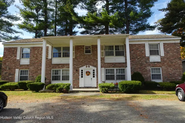 front view of a brick house with a yard and large trees