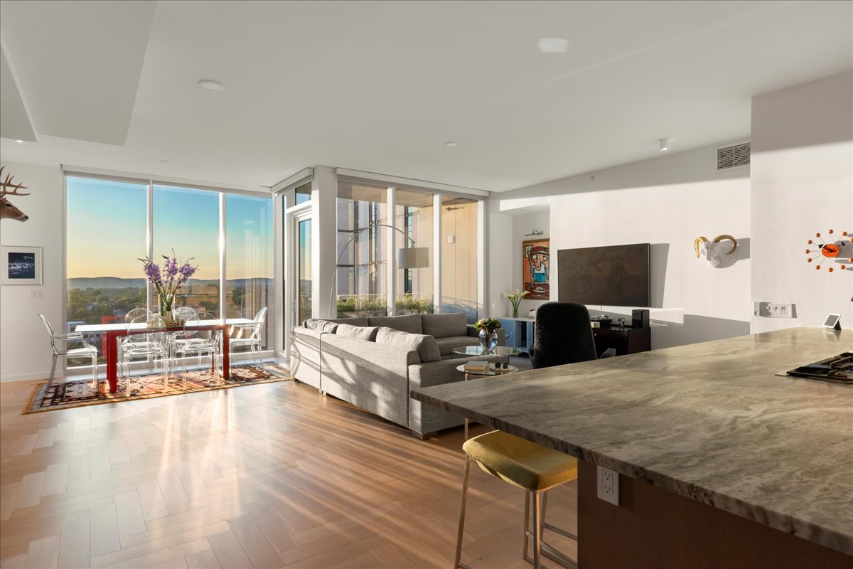313 West 17th Street, Unit 1104 Austin, TX 78701 - Photo 3 of 40 A luminous, corner living space wrapped in floor-to-ceiling glass, capturing panoramic Hill Country and sunset views. The open layout highlights the residence’s upgraded herringbone wood floors and flows naturally into the dining area and terrace, creating an effortless setting for Omakase-style dinners, intimate gatherings or quiet evenings at home.