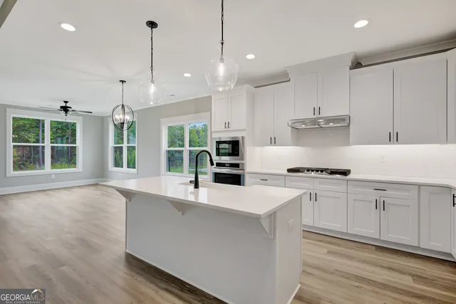 a large kitchen with stainless steel appliances a large counter top a stove a sink and a chandelier