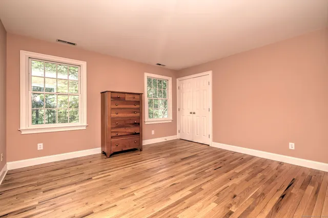 an empty room with wooden floor closet and windows
