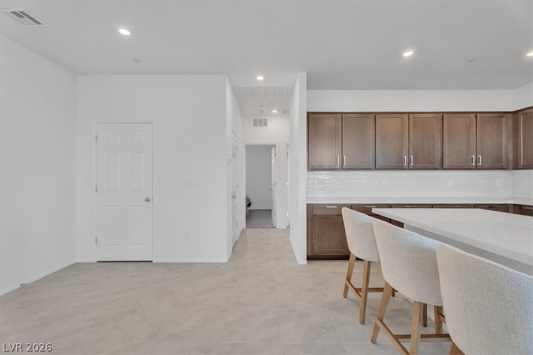 635 Bellus Place Henderson, NV 89015 - Photo 20 of 37 Kitchen with light stone counters, a kitchen breakfast bar, recessed lighting, dark wood finish cabinetry, and tasteful backsplash