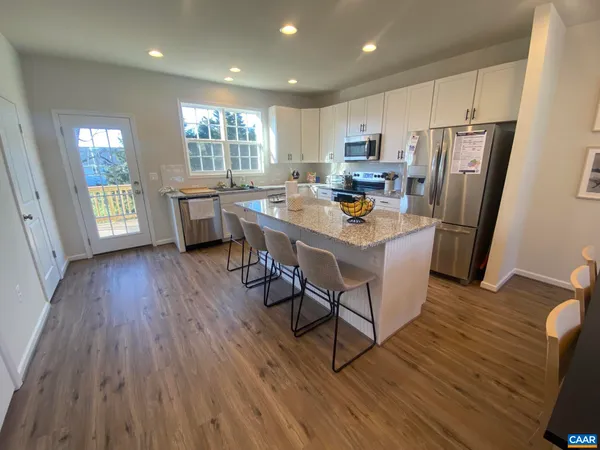 a open kitchen with stainless steel appliances granite countertop a refrigerator a sink dishwasher a stove and a dining table with wooden floor