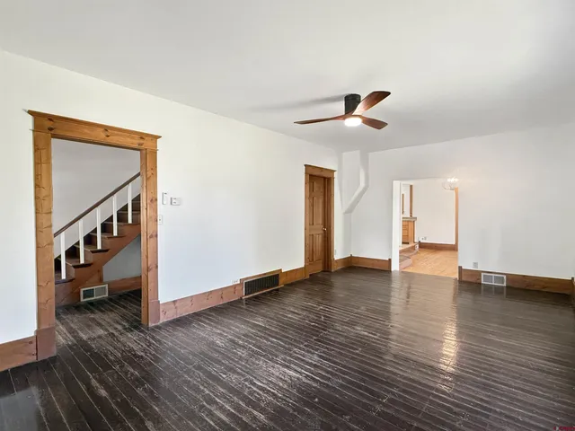 a view of an empty room with wooden floor and a ceiling fan