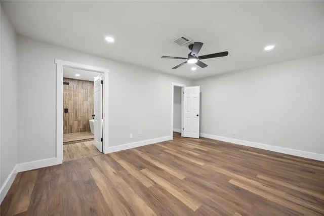 a view of an empty room with wooden floor and a ceiling fan