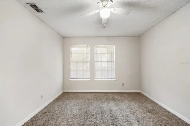 an empty room with a chandelier fan and windows