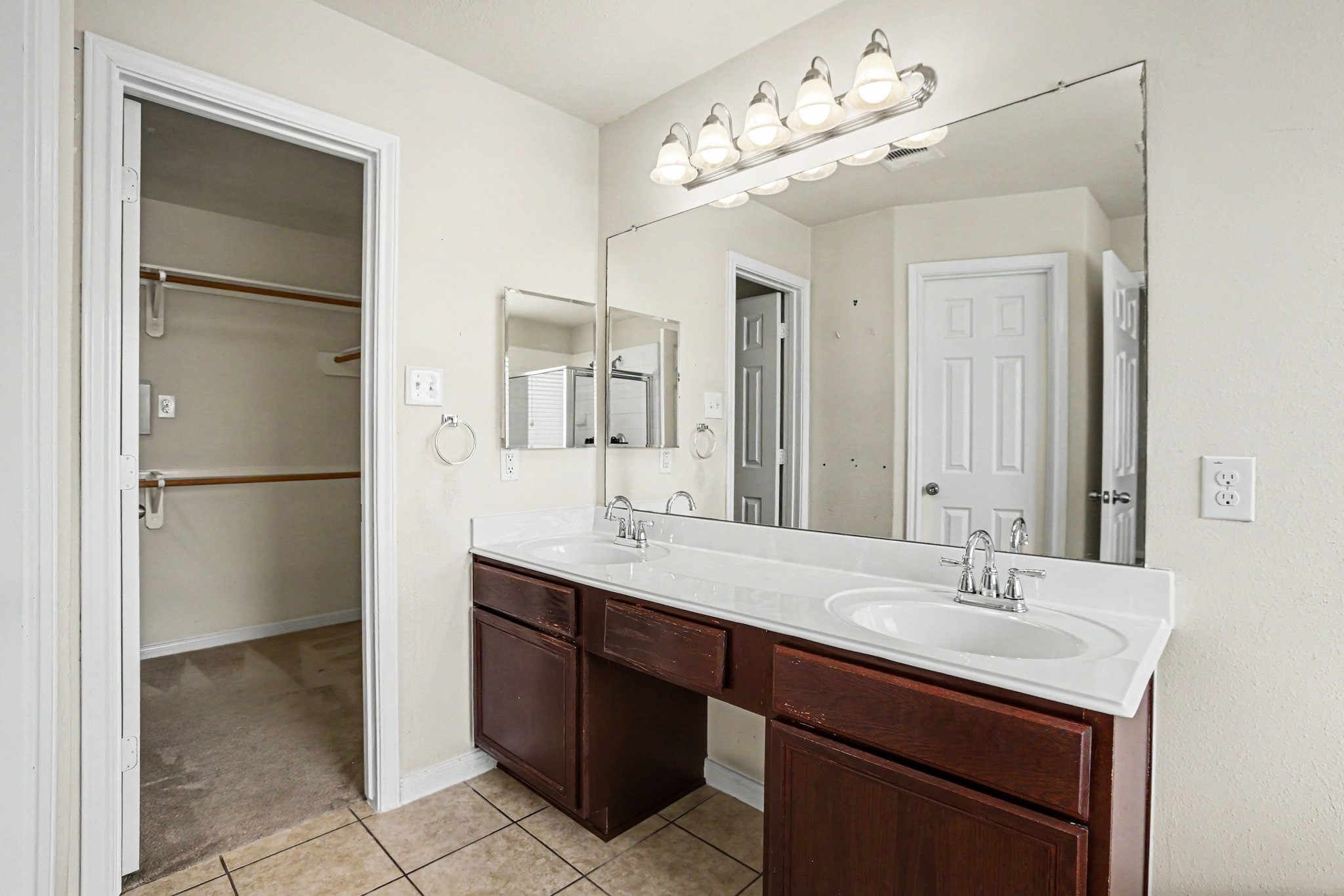 25222 Ginger Ranch Drive Katy, TX 77494 - Photo 24 of 33 Ensuite primary bathroom features a double vanity with dark wood cabinets, a large mirror, and modern lighting. It includes a walk-in closet and neutral tile flooring, offering functionality and style.