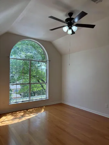 an empty room with wooden floor fan and windows
