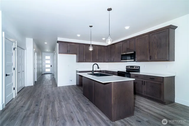 a kitchen with stainless steel appliances granite countertop wooden cabinets a sink dishwasher a stove and a refrigerator with wooden floor