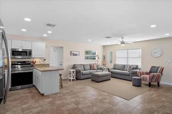 a living room with stainless steel appliances furniture a rug kitchen view and a window