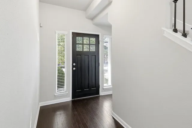 an empty room with wooden floor windows and front door
