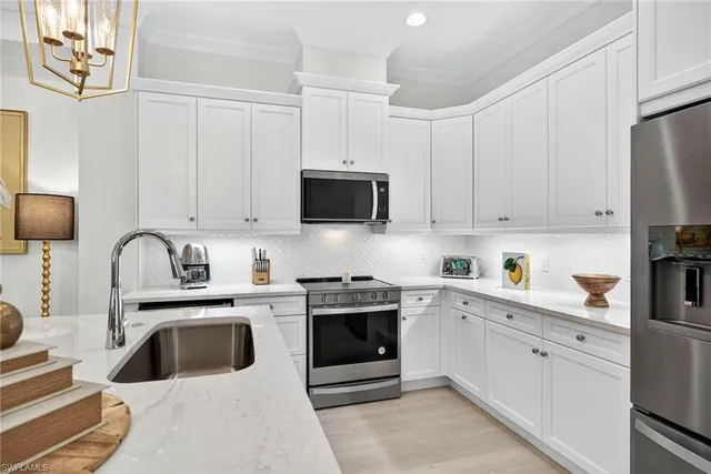 a kitchen with stainless steel appliances granite countertop a sink a stove a refrigerator and white cabinets