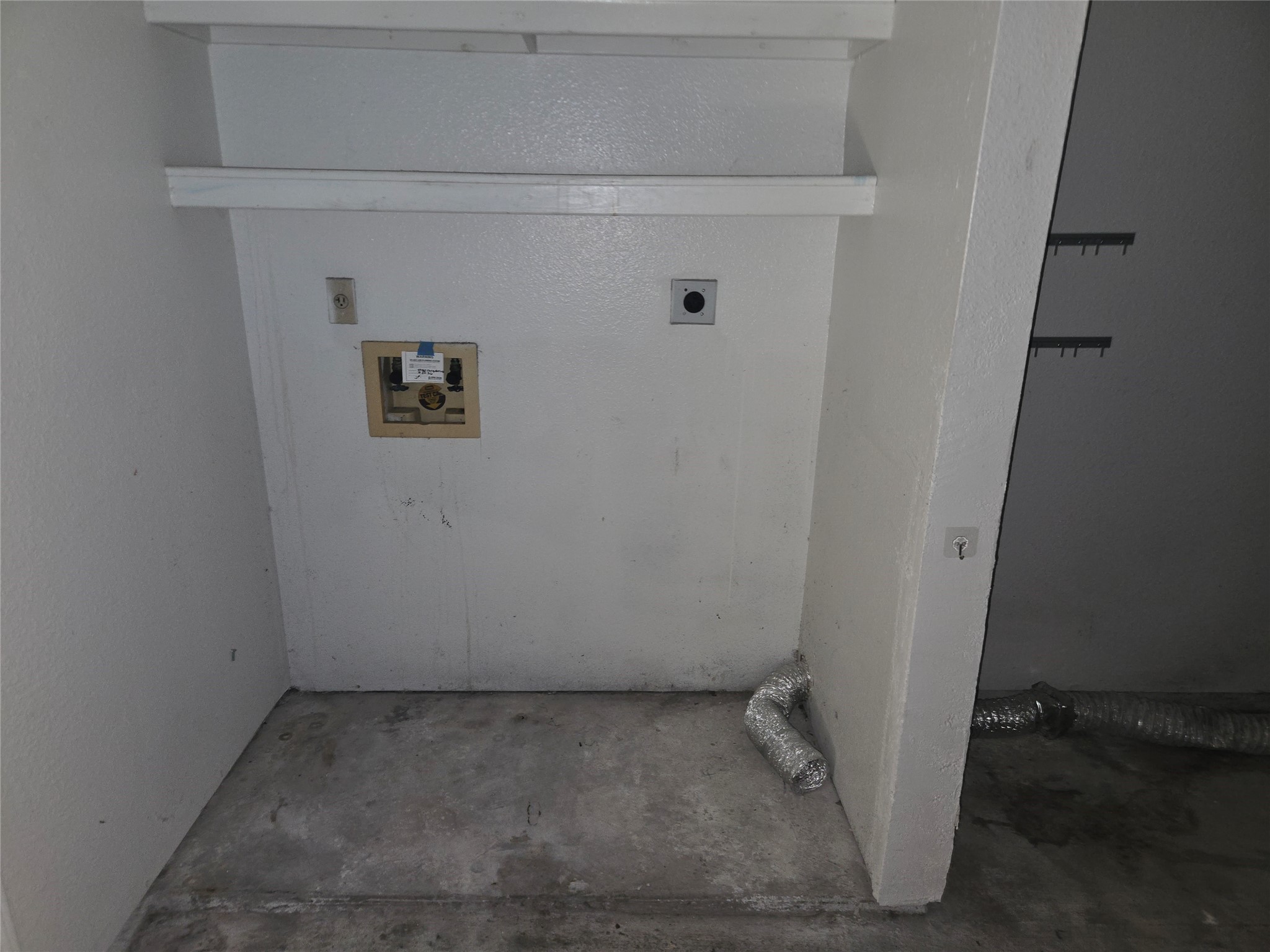 3780 Tanglewilde Street, Unit 501 Houston, TX 77063 - Photo 18 of 26 This photo shows a small laundry area with connections for a washing machine and dryer, concrete flooring, and a wall shelf for storage.