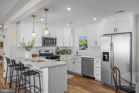 a kitchen with stainless steel appliances a refrigerator a stove a sink cabinets and a dining table with wooden floor