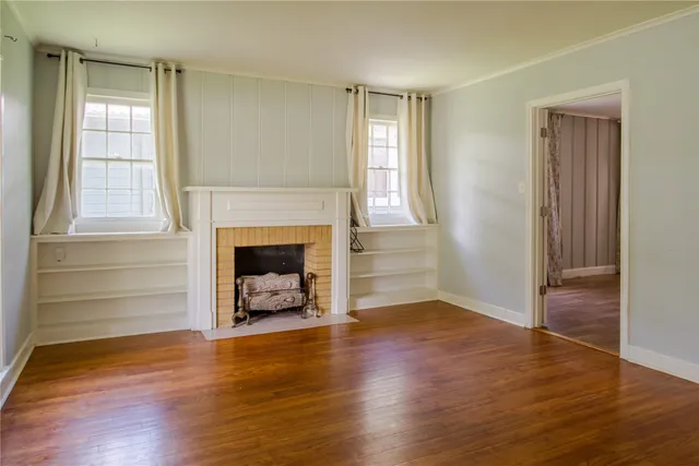 an empty room with wooden floor fireplace and windows