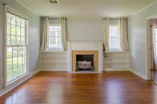 an empty room with wooden floor fireplace and windows