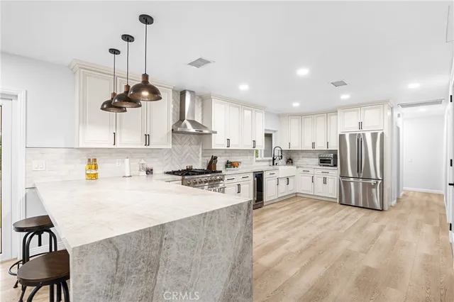 a kitchen with stainless steel appliances a stove a sink a refrigerator a center island and chairs