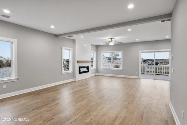 an empty room with wooden floor kitchen view and windows