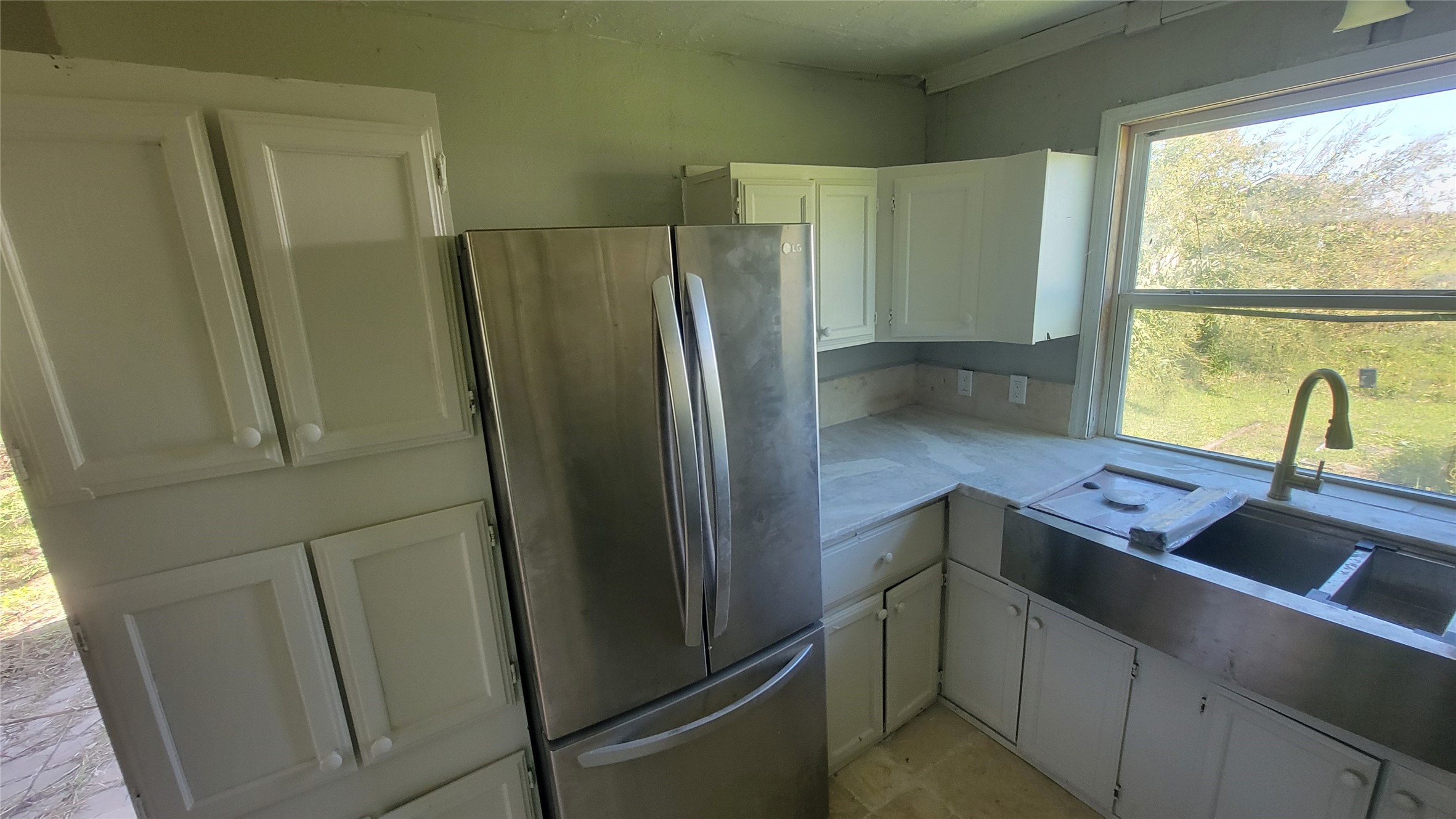 12018 Sandpiper Road Angleton, TX 77515 - Photo 34 of 48 Compact kitchen with stainless steel fridge and sink, white cabinetry, and a large window offering garden views. Needs some updates.