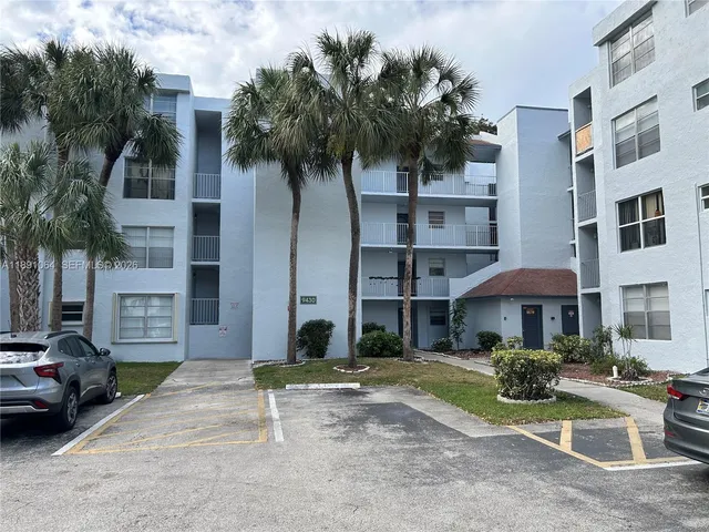 a front view of a building with garden and parking