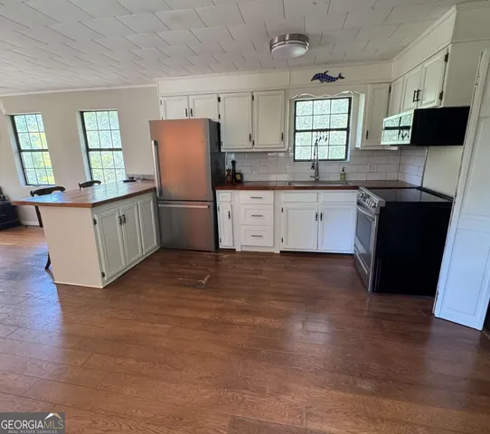 a kitchen with stainless steel appliances granite countertop white cabinets a refrigerator a sink a stove a microwave and wooden floors