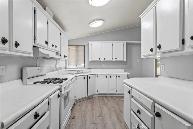 a kitchen with granite countertop a sink stove a refrigerator and white cabinets with wooden floor