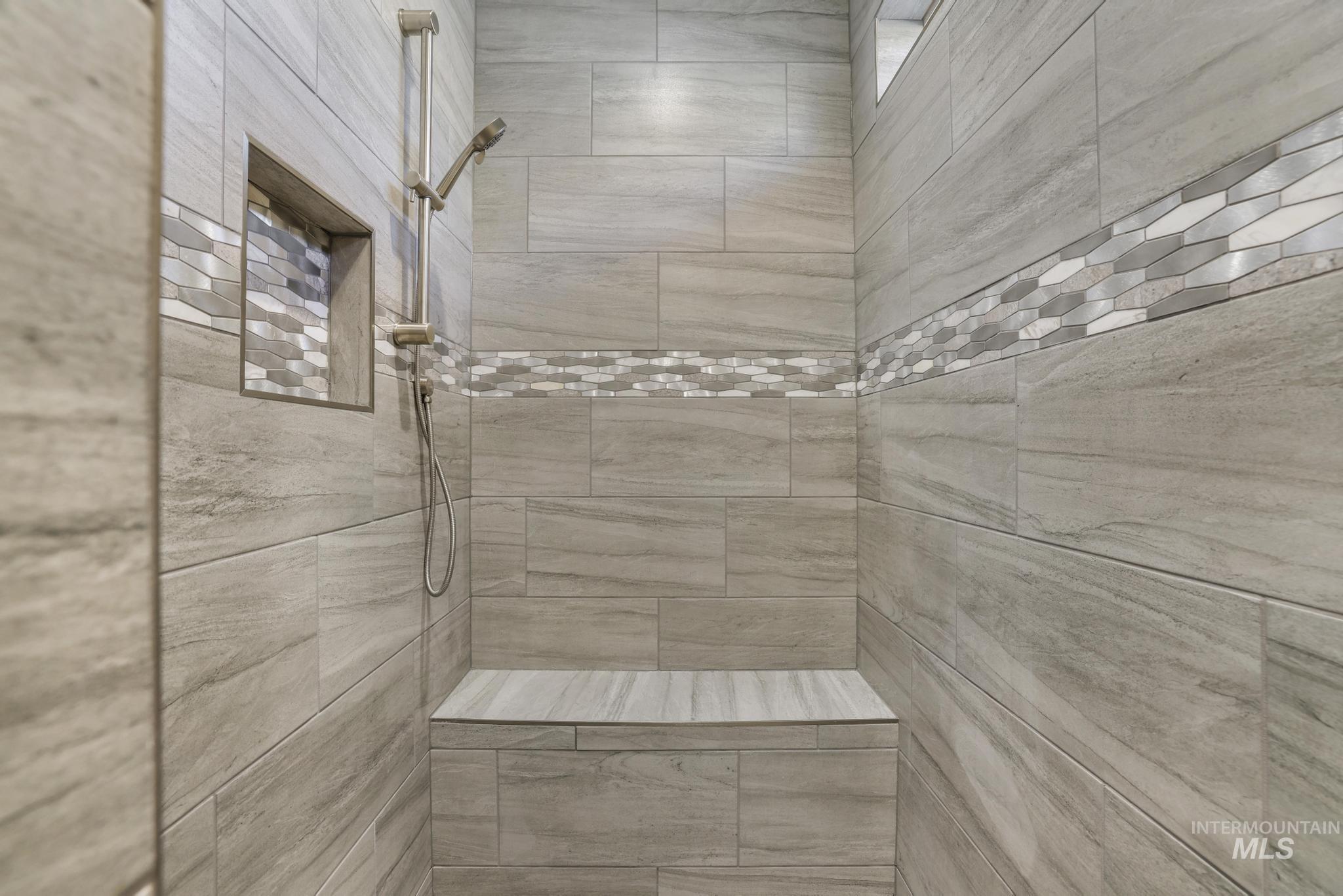 298 Sandi Road Twin Falls, ID 83301 - Photo 17 of 24 Walk-in shower featuring large format gray tile, decorative mosaic accent banding, a built-in shower niche, a handheld shower fixture, and an integrated shower bench