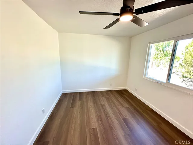an empty room with wooden floor fan and windows