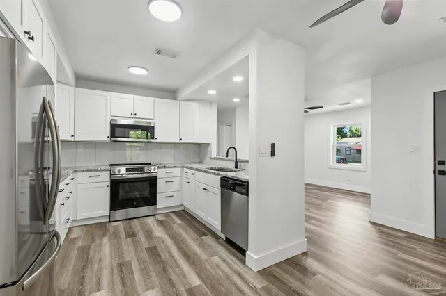 a large kitchen with stainless steel appliances granite countertop a stove top oven a refrigerator a sink and dishwasher with wooden floor