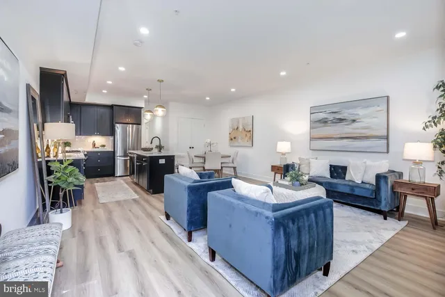 a living room with stainless steel appliances kitchen island granite countertop a refrigerator a sink dishwasher and a dining table with wooden floor