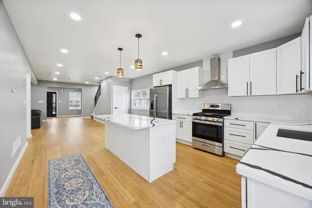 a large kitchen with stainless steel appliances kitchen island granite countertop a stove a sink a refrigerator and white cabinets with wooden floor