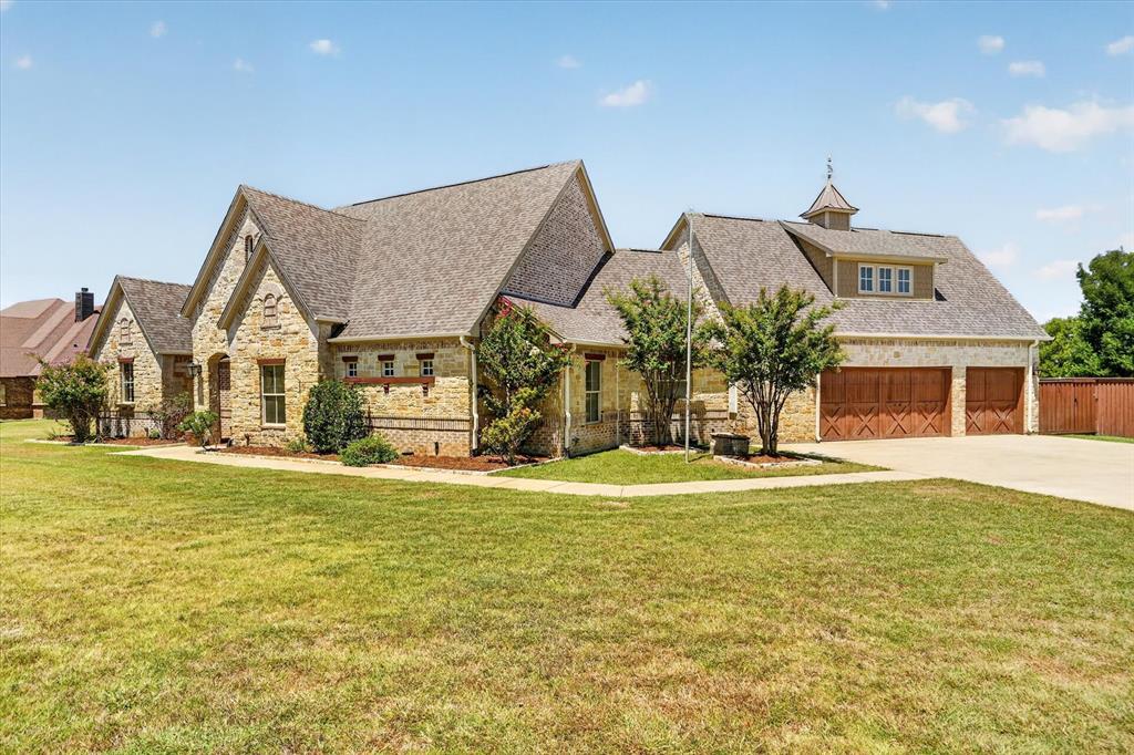Stone exterior with a shingled roof, a three-car garage with wood-finish doors, and a dormer with a cupola