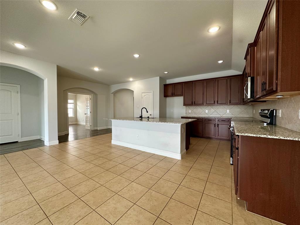 1223 Mount Olive Lane Forney, TX 75126 - Photo 11 of 28 Kitchen with light stone countertops, arched walkways, electric range oven, an island with sink, and recessed lighting