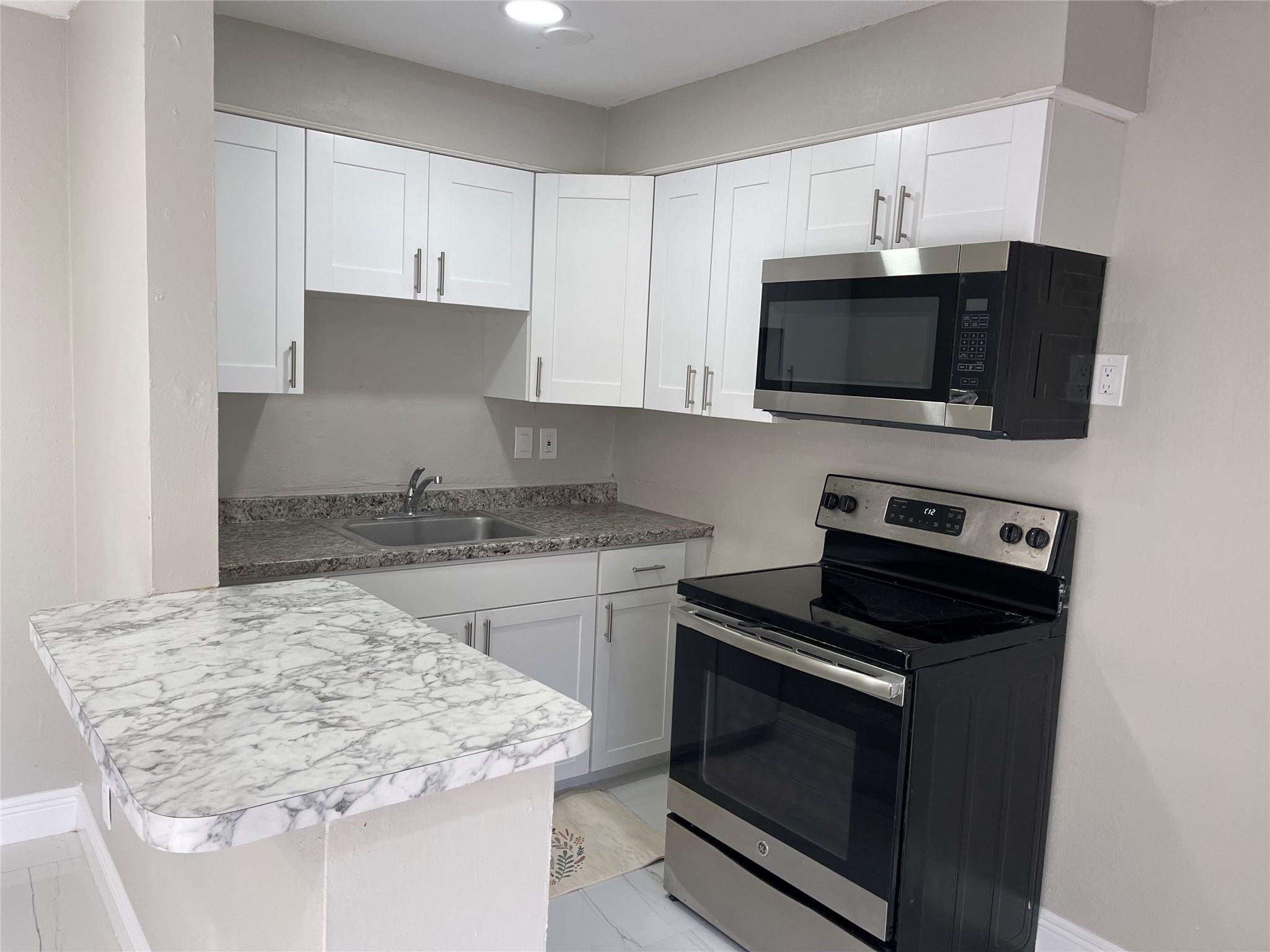 721 Southwest 8th Street Pompano Beach, FL 33060 - Photo 15 of 21 a kitchen with kitchen island granite countertop white cabinets and black appliances