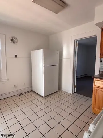 a view of a refrigerator in kitchen and an empty room