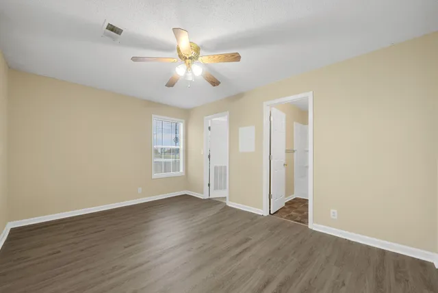 a view of an empty room with wooden floor and a ceiling fan