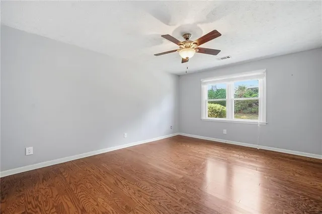 an empty room with wooden floor fan and windows