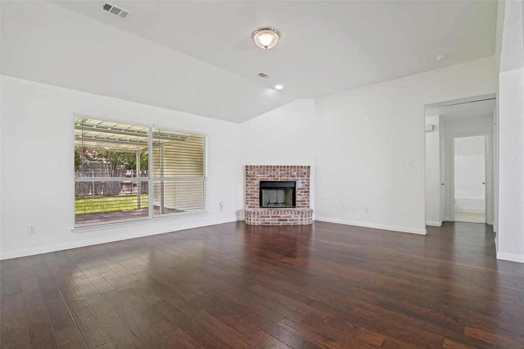 3111 Creekside Drive Sachse, TX 75048 - Photo 5 of 25 Spacious living area featuring wood-finish flooring, a corner brick fireplace, and a large window overlooking a covered patio and backyard
