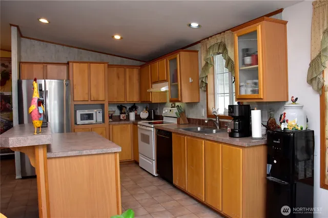 a kitchen with stainless steel appliances granite countertop a refrigerator a sink dishwasher a stove and a dining table with wooden floor