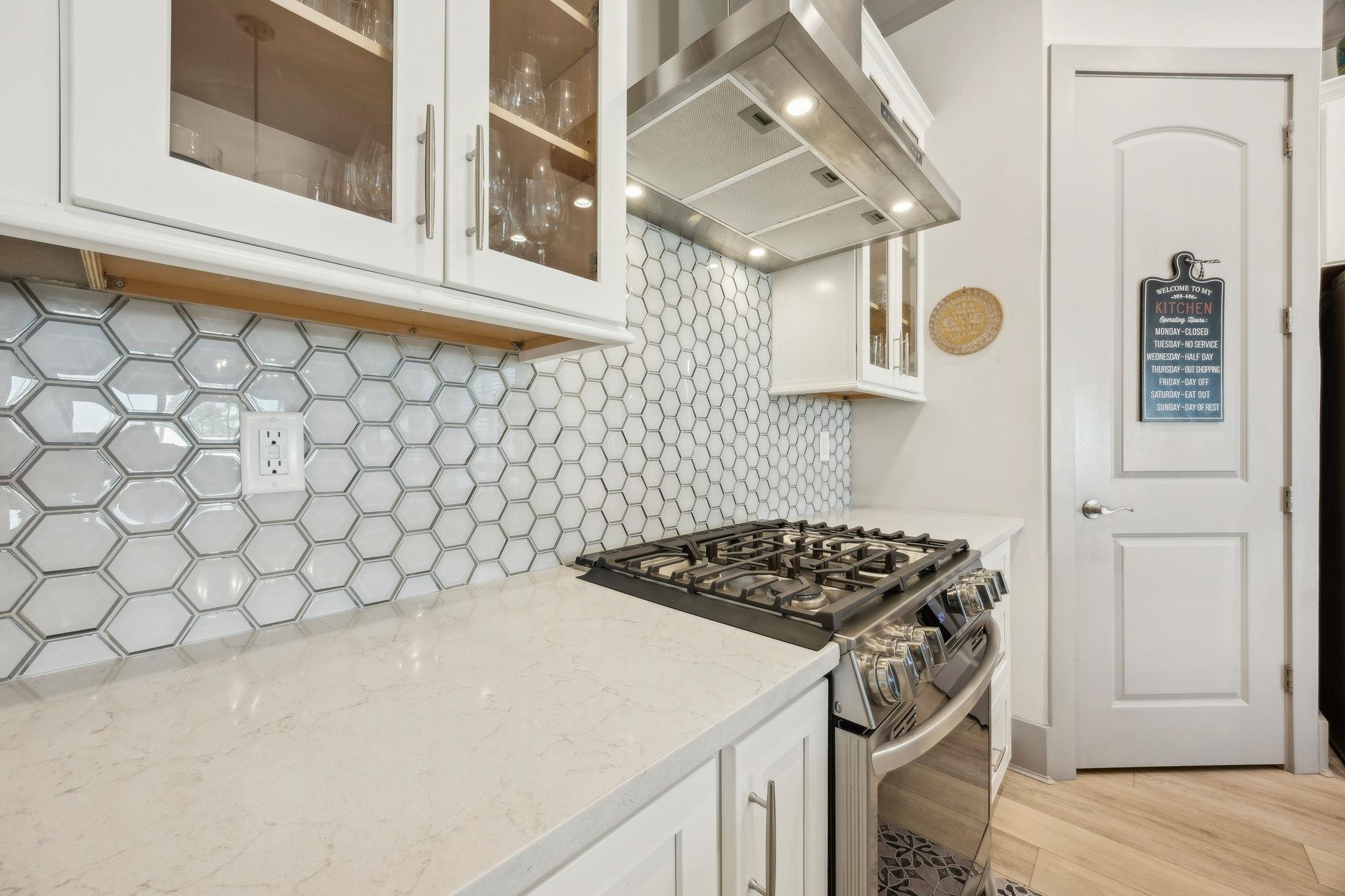 18 Rio Vista Drive Palm Coast, FL 32137 - Photo 13 of 73 Kitchen with stainless steel range with gas stovetop, range hood, white cabinets, glass insert cabinets, and light stone countertops