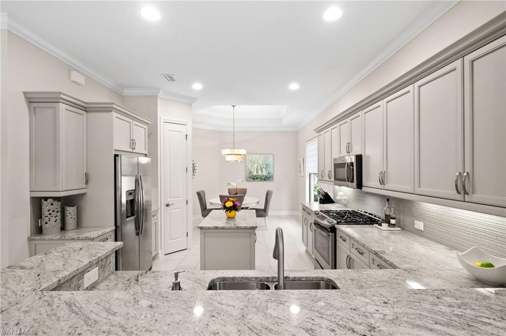 6608 Roma Way Naples, FL 34113 - Photo 5 of 50 Kitchen with light stone countertops, decorative light fixtures, stainless steel appliances, sink, and gray cabinets
