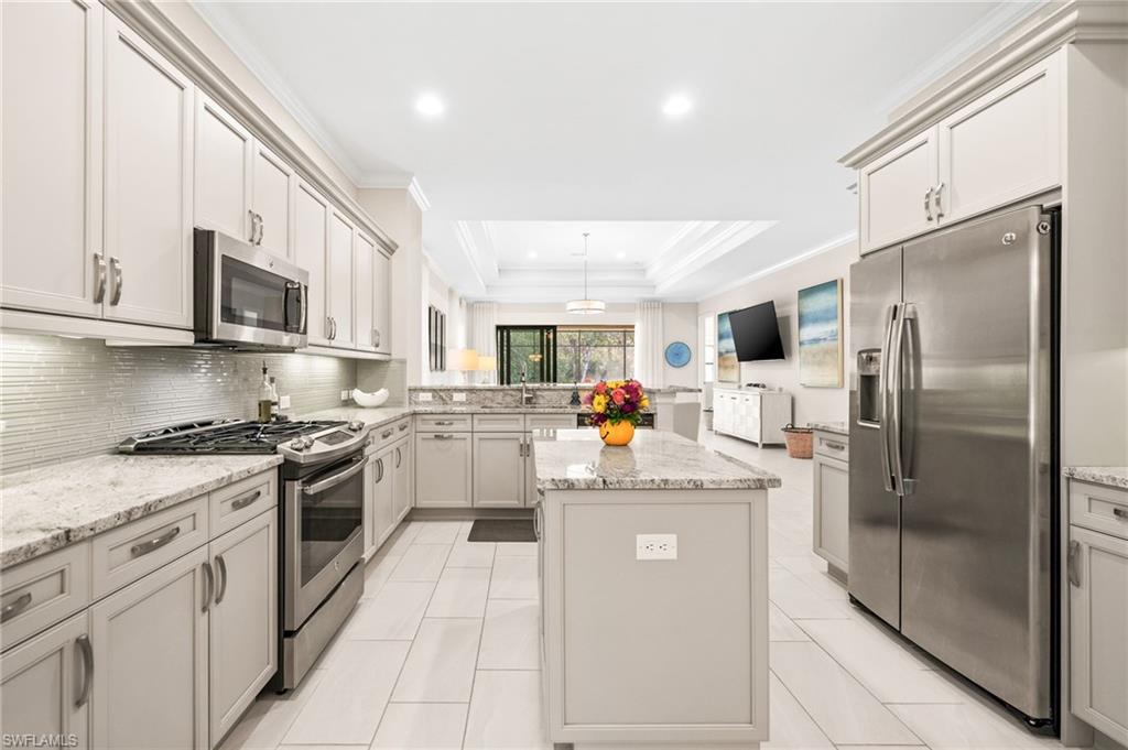 6608 Roma Way Naples, FL 34113 - Photo 7 of 50 Kitchen featuring light stone countertops, appliances with stainless steel finishes, a raised ceiling, and a kitchen island