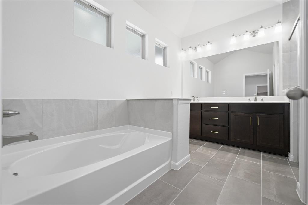 1908 Sangallo Lane Celina, TX 75009 - Photo 17 of 35 Bathroom featuring a white bathtub with a tiled surround, an elongated dark wood-finish vanity with dual sinks, a large wall-mounted mirror, and overhead vanity lighting