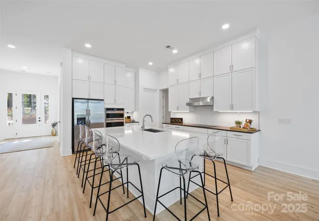 a kitchen with stainless steel appliances granite countertop a stove a sink a refrigerator and white cabinets with wooden floor