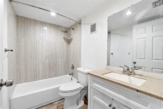 a bathroom with a granite countertop sink a toilet a mirror a bathtub and shower