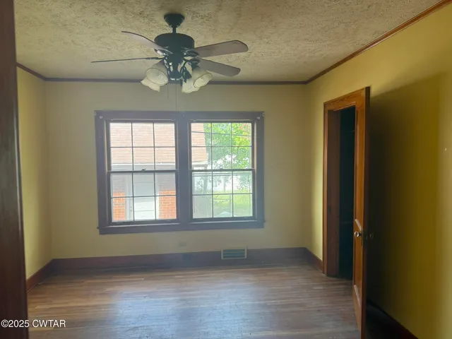 an empty room with wooden floor chandelier fan and windows
