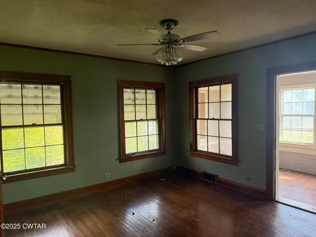 an empty room with wooden floor chandelier and windows