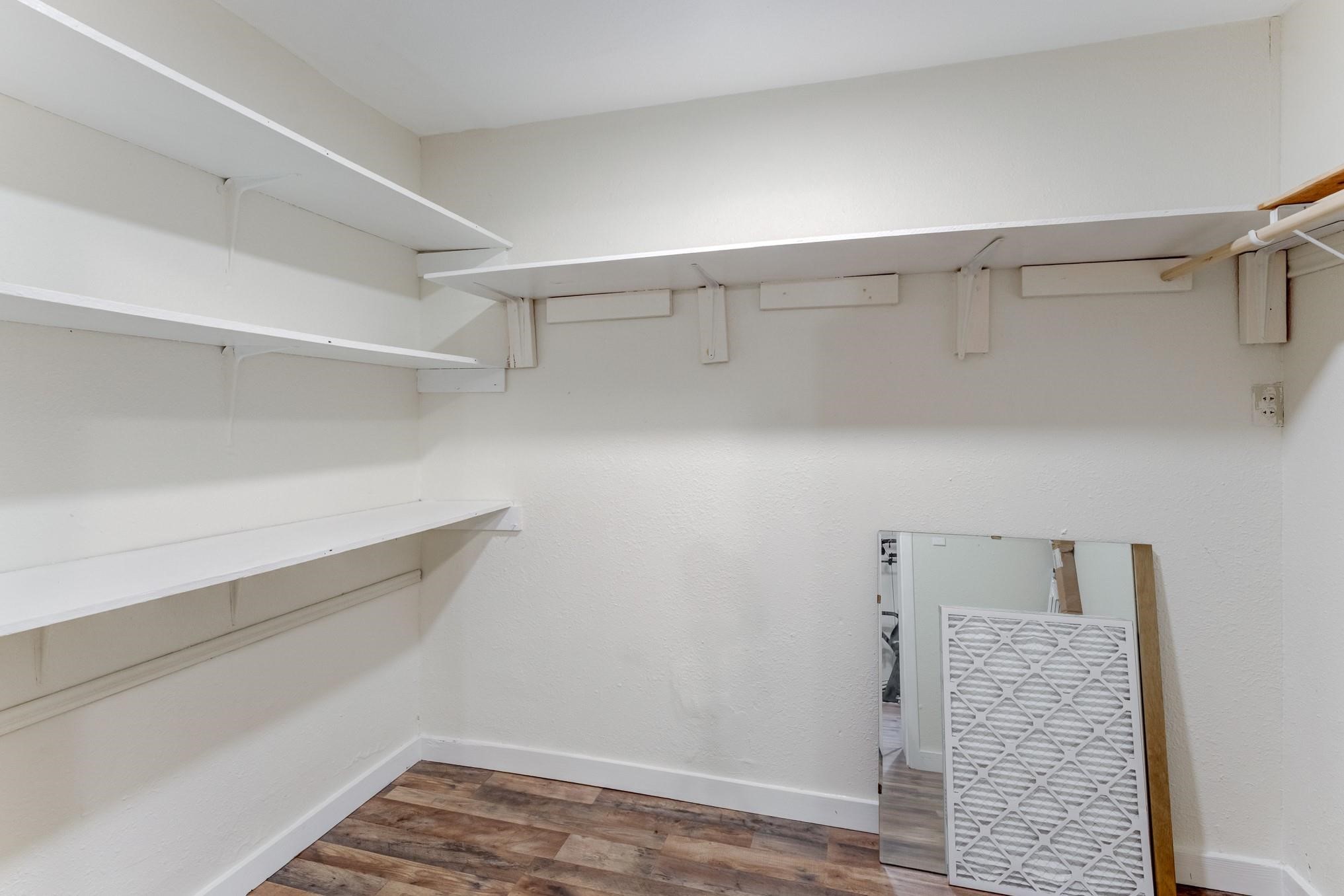 305 Yaupon Street Sweeny, TX 77480 - Photo 8 of 22 This room is a small walk-in closet with white walls and shelving, providing ample storage space. It features wooden flooring and includes a wall-mounted mirror for convenience.