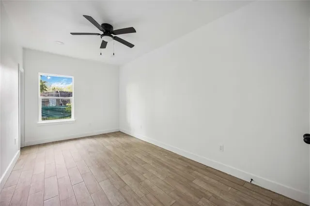 an empty room with wooden floor fan and windows