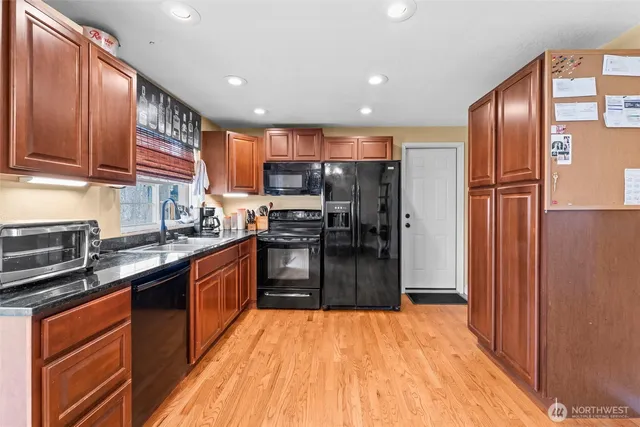 a kitchen with stainless steel appliances granite countertop wooden cabinets a refrigerator a stove a sink and dishwasher with wooden floor