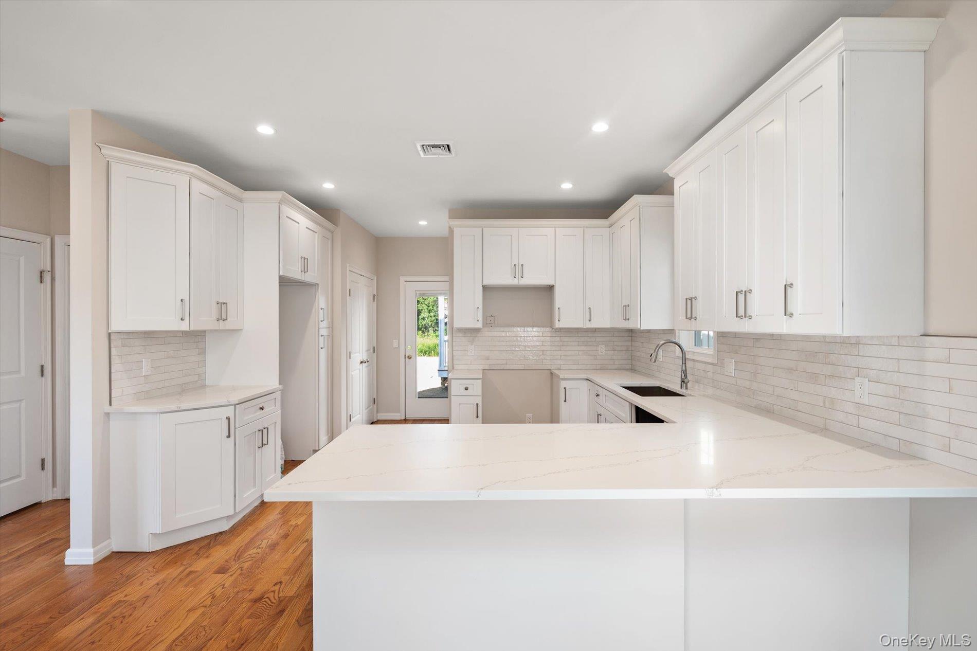 2 Gail-grace Court Copiague, NY 11726 - Photo 12 of 27 Kitchen featuring a peninsula, white cabinets, backsplash, light stone countertops, and light wood-style floors